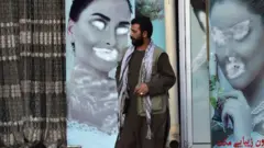 A man stands next to a beauty salon with images of women defaced using spray paint at Shahr-e Naw neighbourhood in Kabul on December 9, 2021.