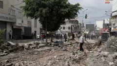 فلسطينيون يتفقدون الأضرار التي خلفتها العملية العسكرية الإسرائيلية التي استمرت عشرة أيام في جنين في الضفة الغربية. ويظهر في الصورة شارع مدمر بالكامل حوله محال تجارية مغلقة.