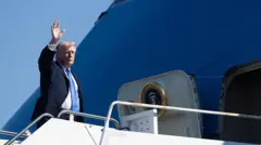 SArışın lacivert takım elbiseli bir adam büyük bir mavi uçağın kapısında el sallıyor. Uçağın kapısında Amerikan başkanlığının logosu var.