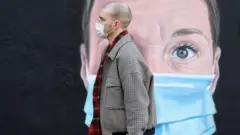 A person wearing a face mask walks past a mural of a nurse in Manchester
