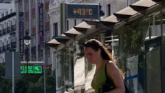 Uma mulher caminha por uma rua em Madri diante de um termômetro que marca 43°C.