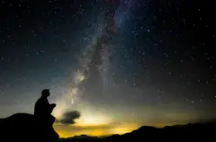 Pessoa sentada em um rochedo observando o céu noturno estrelado