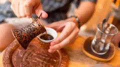 bakır cezveden bir fincana kahve boşaltan bir el ve kenarda bir çay bardağı