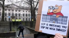 倫敦前皇家鑄幣廠外一名示威者舉起反對中國「超級大使館」用作監視活動的標語牌（8/2/2025）