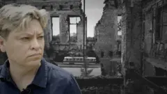 Một người phụ nữ tóc ngắn, mặc áo sơ mi xanh, với phông nền tòa nhà đổ nát ở Kharkiv