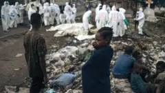 Bamwe mu baturage barimo kureba mu gihe abakozi ba Croix-Rouge barimo guhamba imirambo mu irimbi i Goma ku wa mbere tariki 03 Gashyantare(2) 2025. Ishami rya ONU ry’ubutabazi rivuga ko abantu bagera kuri 900 bapfuye mu mirwano iheruka i Goma