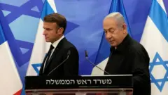 Presidente da França, Emmanuel Macron, ao lado do primeiro-ministro de Israel, Benjamin Netanyahu, em declaração pública, com bandeiras dos dois países ao fundo