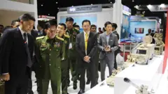  ၂၀၁၉ခုနှစ် ထိုင်းနိုင်ငံမှာကျင်းပတဲ့ စစ်လက်နက်ပြပွဲမှာ ဗိုလ်ချုပ်မှူးကြီးမင်းအောင်လှိုင် နောက်မှာ ကပ်လျက်တွေ့ရတဲ့ နက်ခ်တိုင် အဝါရောင်နဲ့ ဒေါက်တာထွန်းမင်းလတ် 