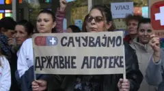 Жена у рукама држи транспарент, протест апотека београд, апотеке београд, протест запослених у апотека београд