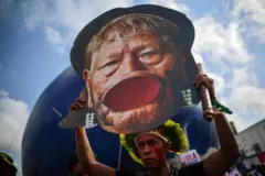 Homem segura cartaz com o rosto de Raoni com seu icônico alargador no lábio inferior, durante protesto na COP30, em Belém