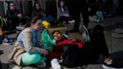 Pessoas sentadas ou deitadas com malas no chão