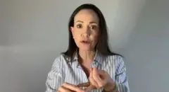 Una mujer de pelo oscuro largo, con una camisa de rayas grises, contra un fondo gris, mirando directamente a cámara