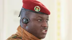 Capt Ibrahim Traoré yambaye umwambwaro wa gisirimkare n'inkofero itukura afise n'agakoresho ko mu gutwi gafasha guhindura indimi 