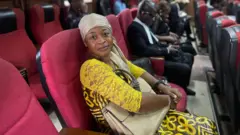 Chioma Okoli in court on Wednesday, 28 October, 2025. She wear yellow dress and grey head scarf wit her bag on top her leg