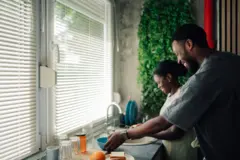 Une femme avec un homme à côté, en train de faire la vaisselle dans une cuisine. Les deux sourient.