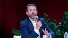Donald Trump Jr, hijo de presidente, con un micrófono en mano, de chaqueta azul y camisa blanca, habla en una conferencia en Sugar Land, Texas. 23 de octubre 2025.