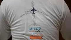 На этой фотографии, сделанной 10 декабря 2025 года, Цзян Хуэй, чья мать находилась на борту пропавшего рейса MH370 авиакомпании Malaysia Airlines, запечатлен в своей квартире в Пекине в футболке, посвященной этой катастрофе.