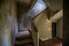 Parte do interior da Casa de Caoba. Uma escada descascada, paredes cobertas de inscrições e sujeira são visíveis.