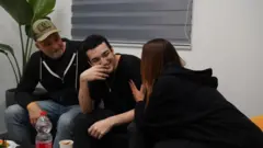 Edan Alexander sonriente en medio de sus dos padres, quienes lo miran con emoción