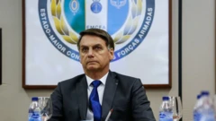 Bolsonaro sentado em reunião, em frente a painel com emblema das Forças Armadas