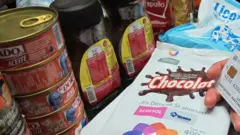 A mão de um consumidor segura um cartão de crédito no caixa, cercado por mantimentos