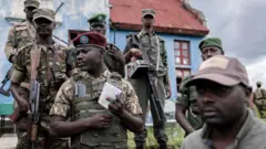 Col John Imani Nzenze wa M23 (wambaye ingoferi itukura) hamwe n'abamurinda kuwa gatanu bashyikiriza ingabo z'akarere ikigo cya gisirikare cya Rumangabo