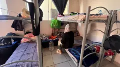 Shukriah sits on a bunk bed with her back to camera