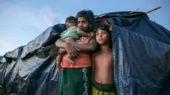 A Rohingya refugee family stands by their makeshift home in Bangladesh