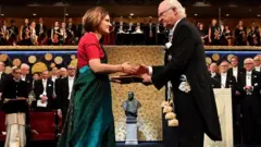 সুইডেনের রাজার কাছ থেকে শাড়ি পরে নোবেল পুরস্কার গ্রহণ করছেন অর্থনীতিবিদ এসথার ডুফলো