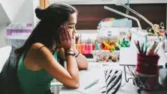 गालामा हात राखेर काम गर्ने कुर्सीमा बसिरहेकी एक महिला