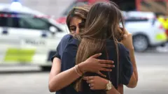 Two distressed women hug outside a Copenhagen shopping centre