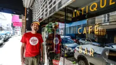 Guto Lima em frente a fachada de sua loja, com vidro escrito 'Antique Café'
