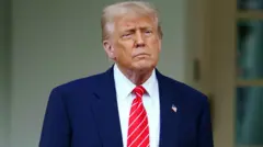 Donald Trump, wearing a blue suit and red and white striped tie, looks off to the side