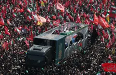 جنازه علی خامنه‌ای در یک لاری قرار دارد و توسط هزاران نفر احاطه شده است. 