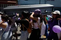 Mulheres carregam caixão escuro para sepultamento