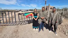 Três pessoas de pé em frente a uma porteira