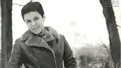 Elis sorrindo para foto, próxima de árvores