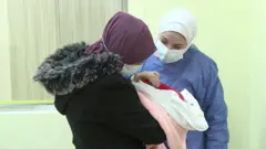 نور والدة التوأمين وهي تحمل واحدة منهما