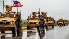 Tanklar, üzerlerinde Amerikan bayrakları var, önde motorsikletli bir Suriyeli 
