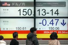 Japanese people pass in front of a screen showing the yen's exchange rate against the dollar