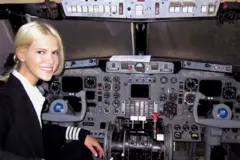 Nadia Marcinko em um uniforme de piloto sentada na cabine de uma aeronave cheia de controles, instrumentos e controles duplos.