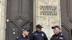 Trojica policajaca stoje u uniformama ispred zgrade rektorata u Beogradu, iznad njih je natpis Univerzitet u Beogradu