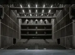 Auditorio amplio visto desde el escenario, con varias balconadas, paredes acústicas oscuras y un techo iluminado con estructura metálica.
