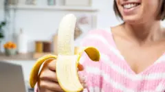 زنی خندان موزی را در دست گرفته