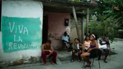 Família cubana, em casa pobre com a frase "Viva a Revolução" em espanhol, pintada em uma parede