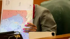 Una persona, con el rostro oculto, mira un documento en cuyo reverso hay un mapa que muestra un plan para la redistribución de los distritos de Texas.