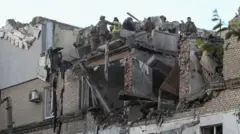 Bombeiros estão sobre um prédio residencial destruído em Dnipro, na Ucrânia, após uma série de ataques russos durante a madrugada