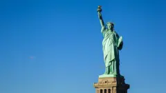 A Estátua da Liberdade, inteira no seu pedestal, em dia ensolarado e sem nuvens no céu