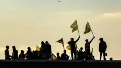 يلوح أكراد سوريون بأعلام تحمل صور مؤسس حزب العمال الكردستاني (PKK)، عبد الله أوجلان، أثناء تجمعهم في مدينة القامشلي ذات الأغلبية الكردية شمال شرق سوريا للاستماع إلى رسالة من الزعيم المسجون في 27 فبراير/شباط 2025. وكان أوجلان قد أصدر دعوة تاريخية في 27 فبراير/شباط لتفكيك قواته المسلحة الكردية، ولمقاتليه لإلقاء السلاح.