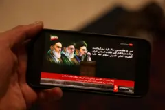 رجل يتابع عبر هاتفه، في 4 يونيو/حزيران 2026، بثاً مباشراً لمسؤول إيراني يقرأ رسالة من المرشد الأعلى مجتبى خامنئي أمام ضريح مؤسس الجمهورية الإسلامية روح الله الخميني في طهران.